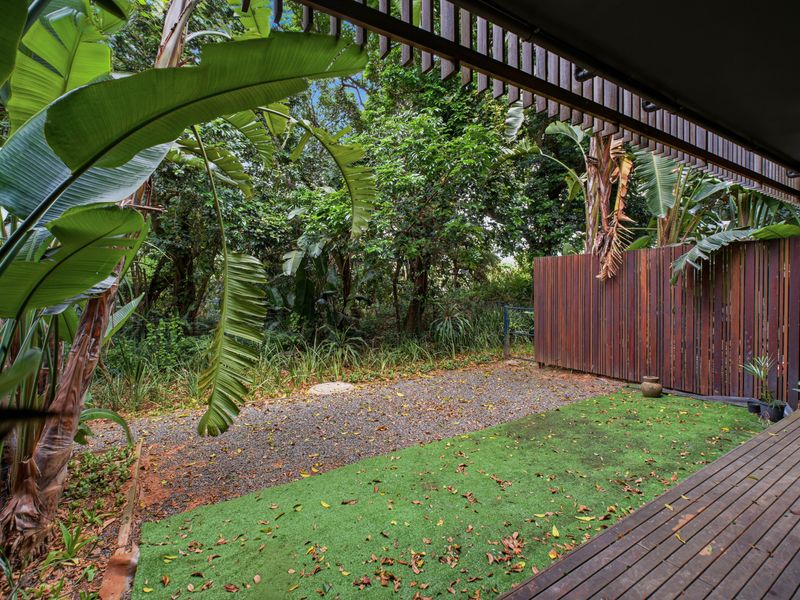 A private outdoor patio featuring timber decking, a slatted privacy screen, and a combination of artificial turf and gravel, overlooking a lush garden area.