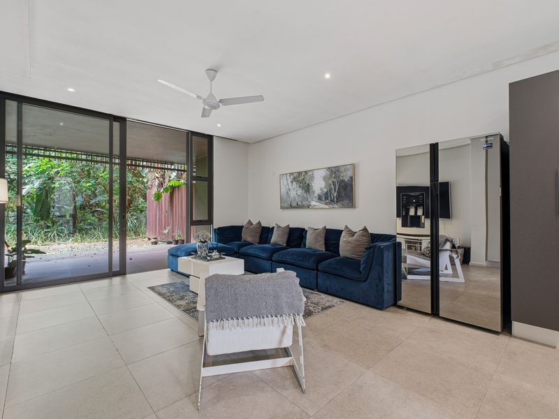 Spacious living area featuring large sliding glass doors that open to a private garden, complemented by neutral tiled flooring and modern recessed lighting.