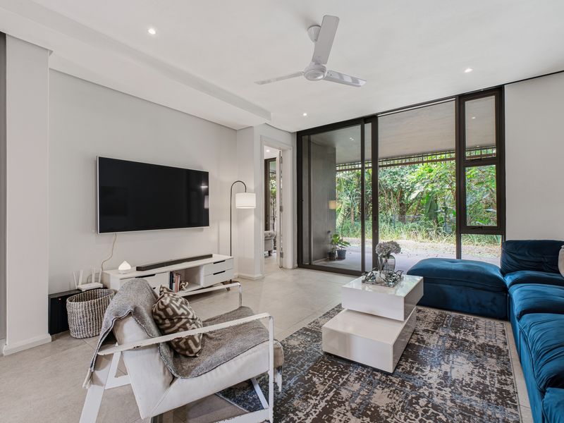 Modern living room featuring tiled flooring, recessed lighting, a ceiling fan, and large sliding glass doors opening to a lush outdoor area.