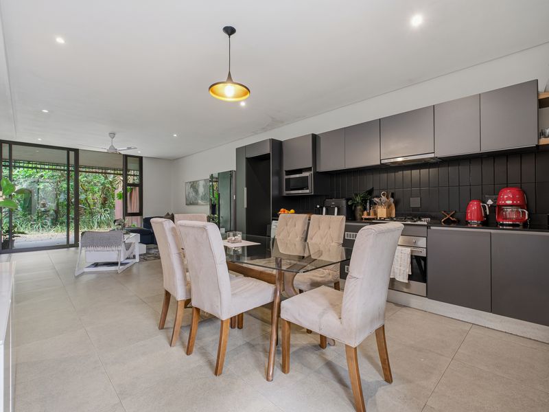 Modern open-plan kitchen and dining area featuring sleek dark cabinetry, integrated appliances, tiled floors, and seamless access to the outdoor patio through sliding doors.