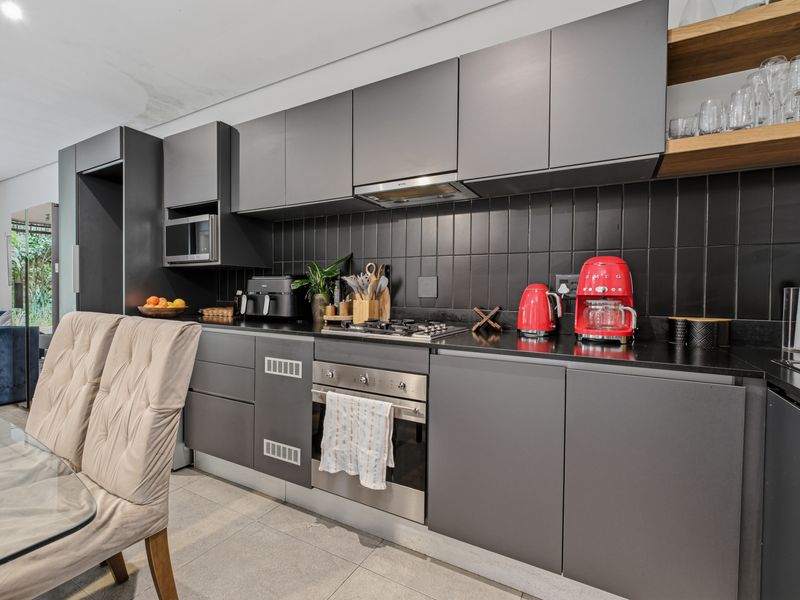Modern open-plan kitchen featuring dark matte cabinetry, stone countertops, integrated appliances, and a tiled backsplash, seamlessly flowing into the dining area.