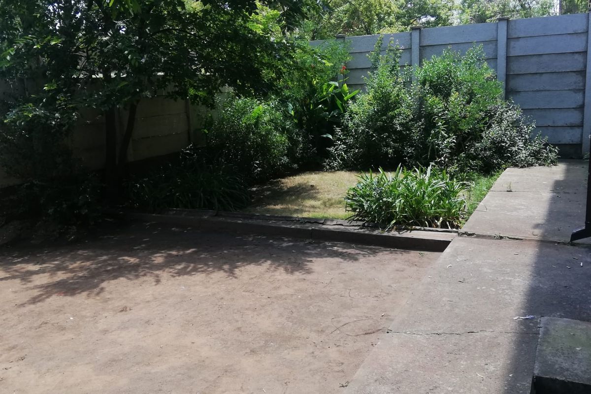 A private rear garden area featuring a concrete patio slab, established trees, and a precast concrete boundary wall.