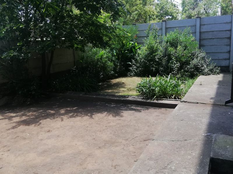 A private rear garden area featuring a concrete patio slab, established trees, and a precast concrete boundary wall.