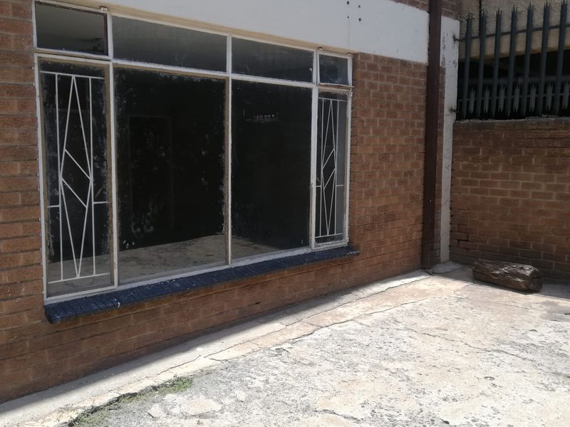 Rear exterior view of the flat featuring a brick facade, security-barred windows, and a concrete patio area with visible signs of wear.