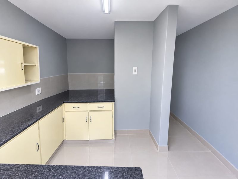 A clean, empty kitchen area featuring granite countertops, light-colored built-in cabinetry, and neutral tiled flooring with a modern grey wall finish.