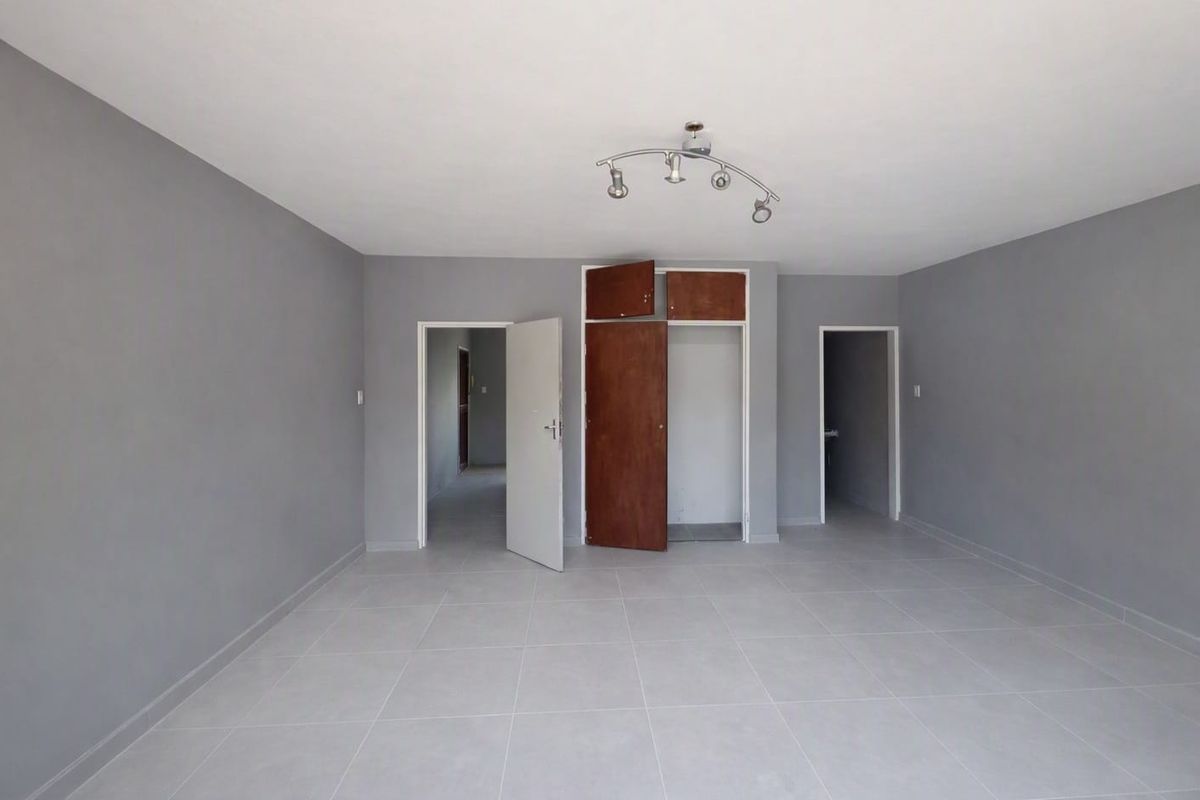 An empty living room featuring neutral grey walls, tiled flooring, and a built-in storage cupboard with overhead compartments.