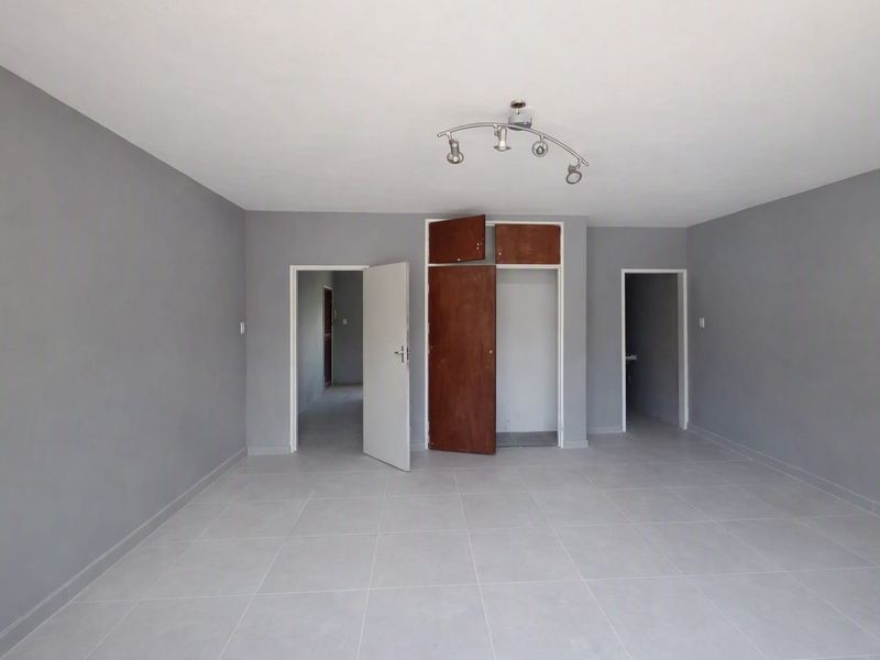 An empty living room featuring neutral grey walls, tiled flooring, and a built-in storage cupboard with overhead compartments.