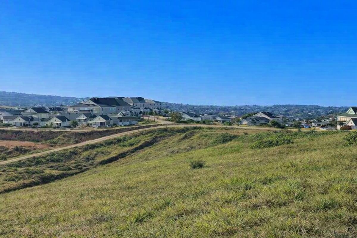 A wide-angle view of a sloped, grassy vacant residential plot overlooking a developed suburban estate.