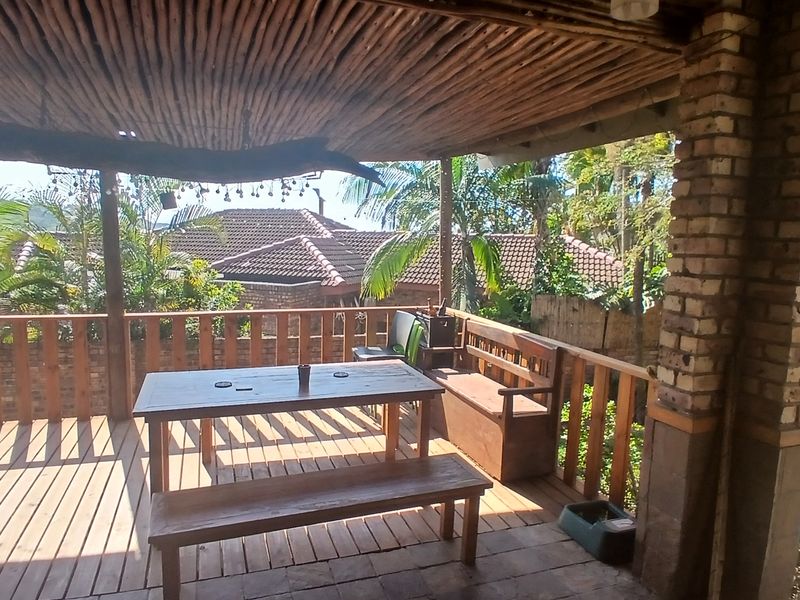 Covered outdoor patio featuring timber decking, a rustic thatched roof, and brick support pillars, overlooking the garden area.