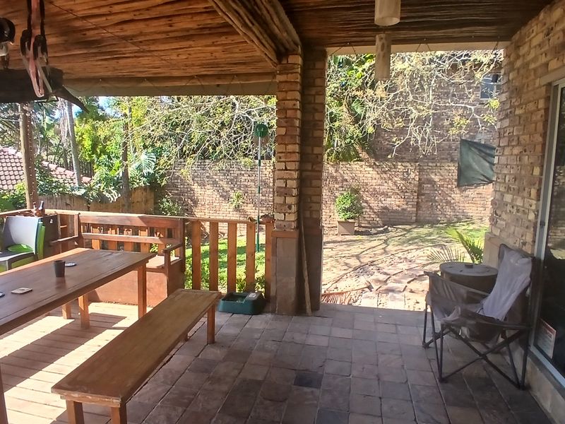 A covered outdoor patio featuring a thatched roof, brick pillars, and tiled flooring, providing direct access to the rear garden area.