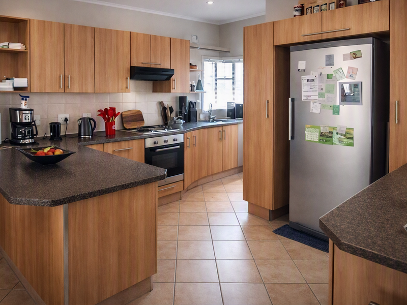 A functional kitchen featuring wood-look laminate cabinetry, dark laminate countertops, built-in oven with gas hob, and tiled flooring throughout.