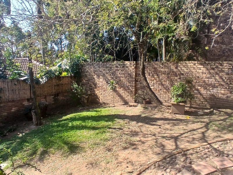 A private garden area featuring a brick boundary wall, mature trees, and a stone paved pathway, offering potential for landscaping improvements.