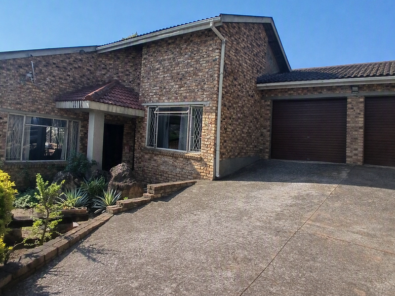 Front elevation of a face brick house featuring a double garage, concrete driveway, and established garden area.