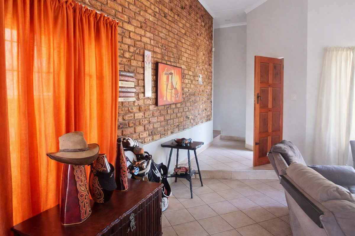 Living area featuring a prominent exposed brick feature wall, tiled flooring, and a traditional timber door leading to an adjacent space.
