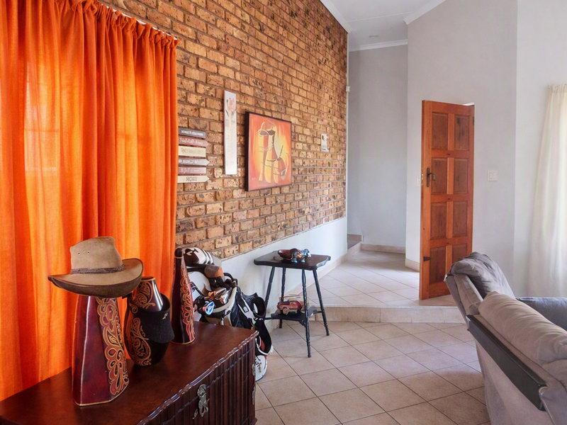 Living area featuring a prominent exposed brick feature wall, tiled flooring, and a traditional timber door leading to an adjacent space.