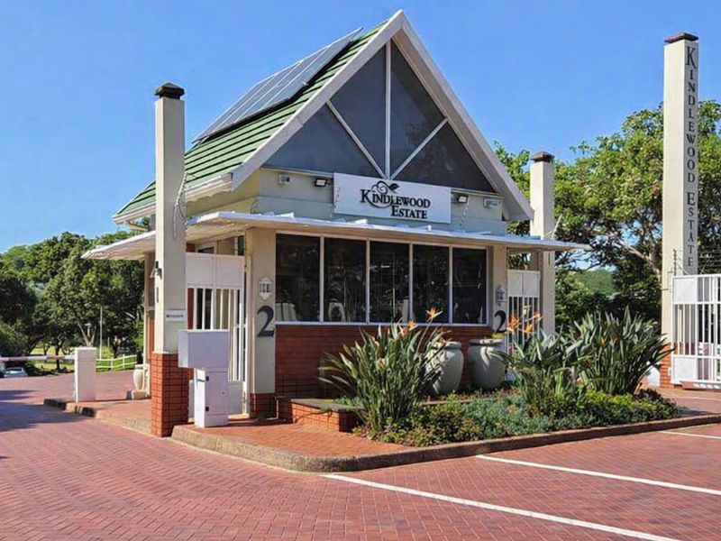 The entrance to Kindlewood Estate featuring a well-maintained security gatehouse, brick paved driveway, and integrated solar panels.