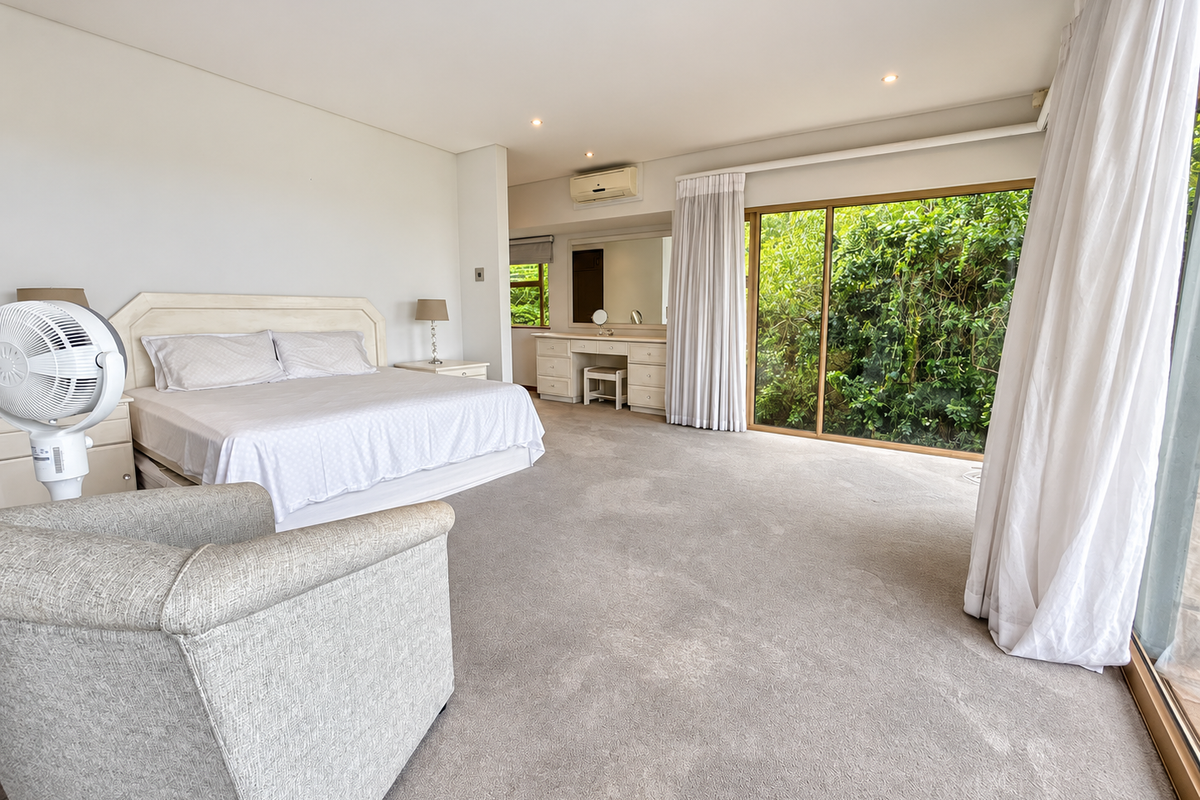 Spacious bedroom featuring neutral carpeting, a built-in vanity, wall-mounted air conditioning, and large sliding glass doors providing access to the garden.