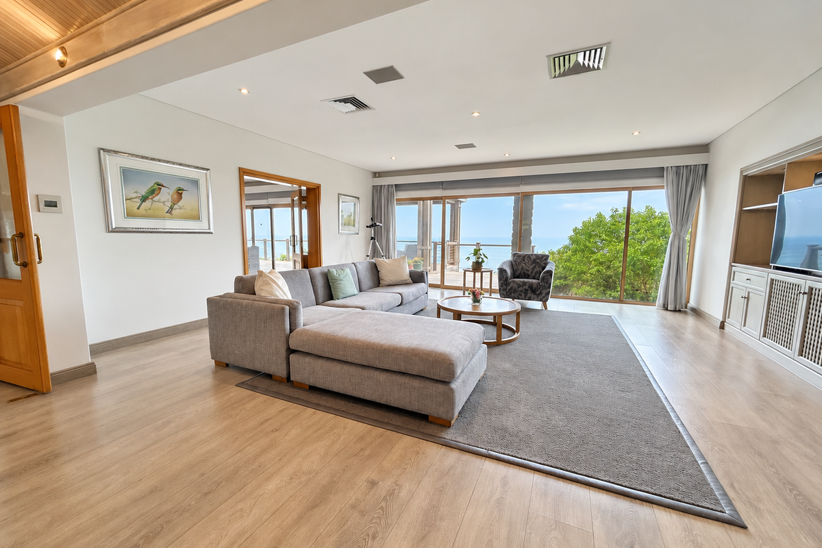 Spacious living room featuring light wood-look flooring, recessed lighting, built-in cabinetry, and large sliding glass doors opening to an outdoor balcony with ocean views.