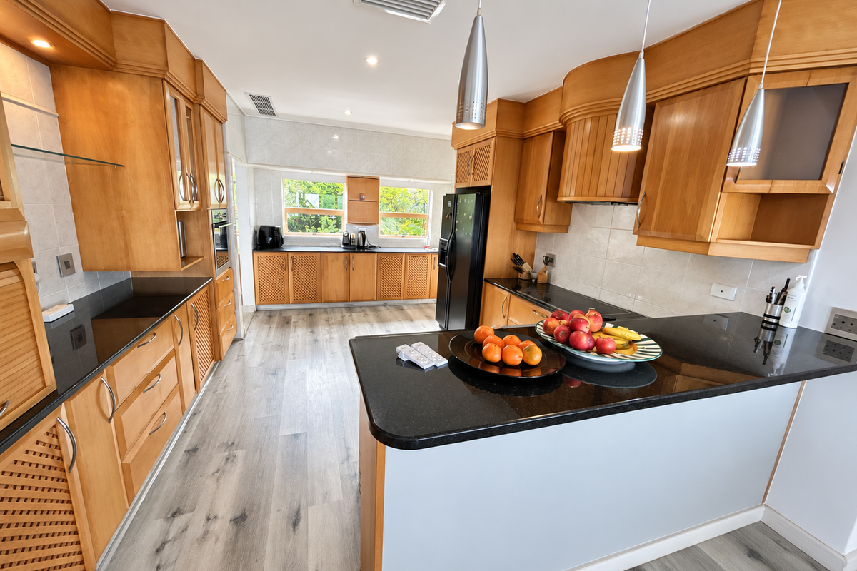 Spacious kitchen featuring warm-toned wooden cabinetry, contrasting black granite countertops, modern laminate flooring, and integrated appliances with stylish pendant lighting.