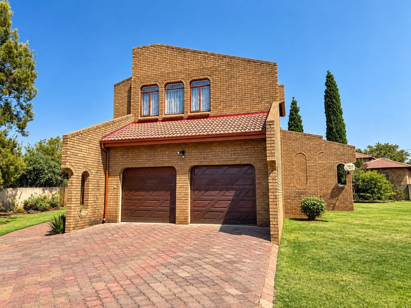 Front view of a double-story brick house featuring a double garage, paved driveway, and well-maintained garden.
