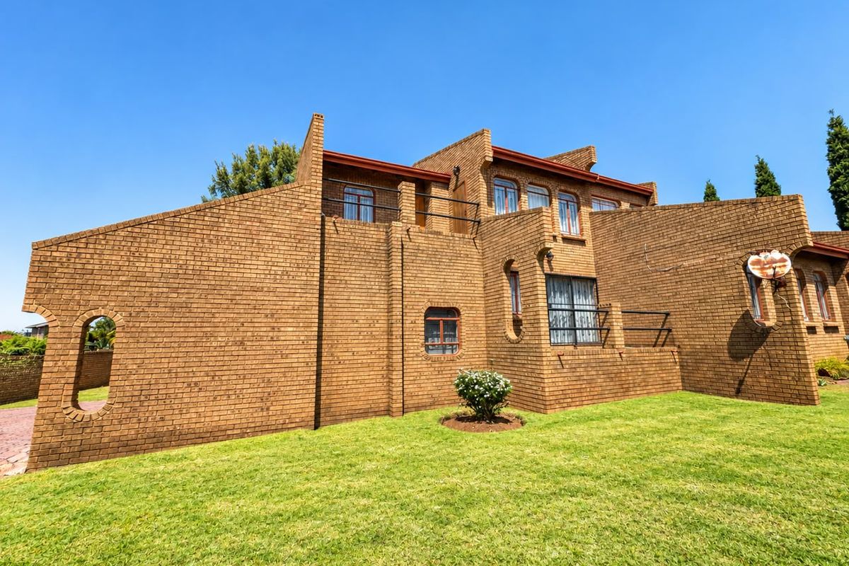 Rear view of a multi-level face brick house featuring arched windows, a balcony with metal railings, and a well-maintained lawn.