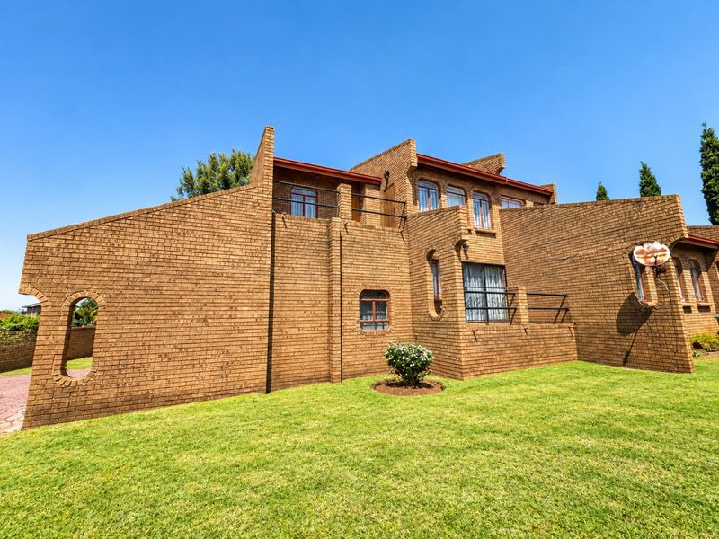Rear view of a multi-level face brick house featuring arched windows, a balcony with metal railings, and a well-maintained lawn.