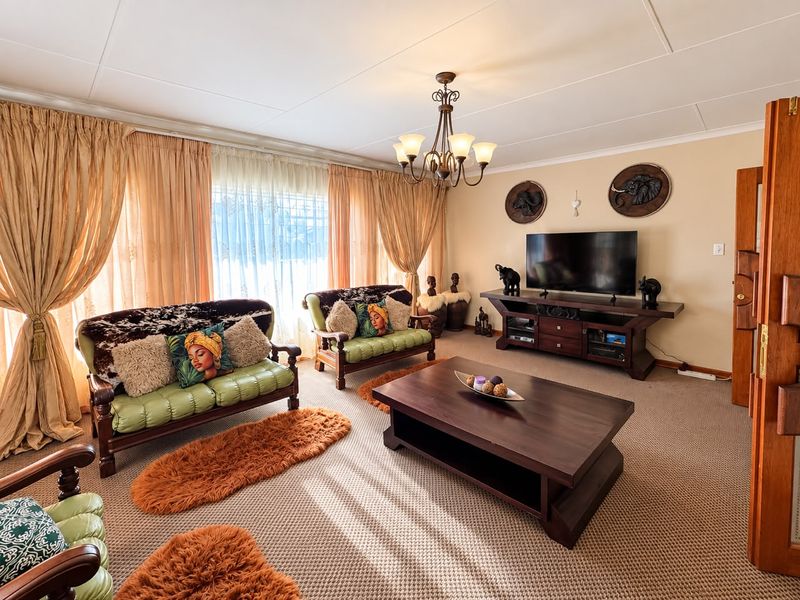 A spacious living room featuring carpeted flooring, a central chandelier, and large sliding glass doors that provide ample natural light.