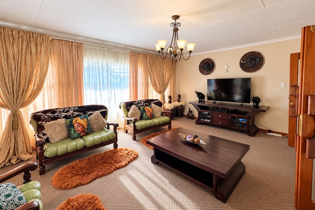 A spacious living room featuring carpeted flooring, a central chandelier, and large sliding glass doors that provide ample natural light.