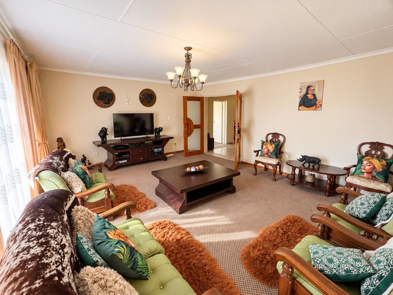 A spacious living room featuring carpeted flooring, a central chandelier, and double doors leading to an adjacent hallway.