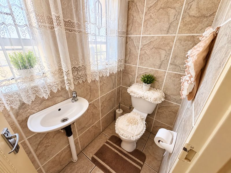 A compact guest bathroom featuring neutral ceramic wall and floor tiling, a wall-mounted basin, and a standard toilet.