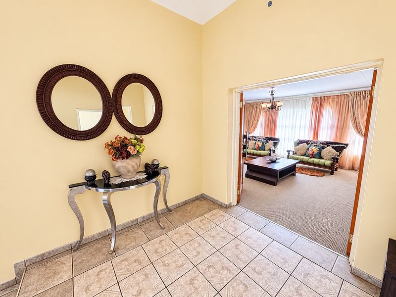 A bright entrance foyer featuring tiled flooring, leading through a wide doorway into a carpeted living area.