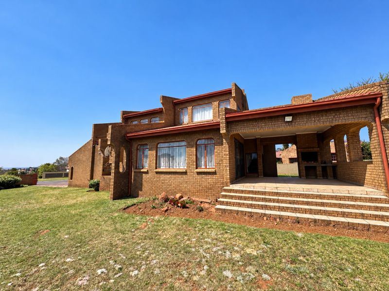 Rear view of a face brick house featuring a covered patio with a built-in braai and tiled steps leading to the garden.
