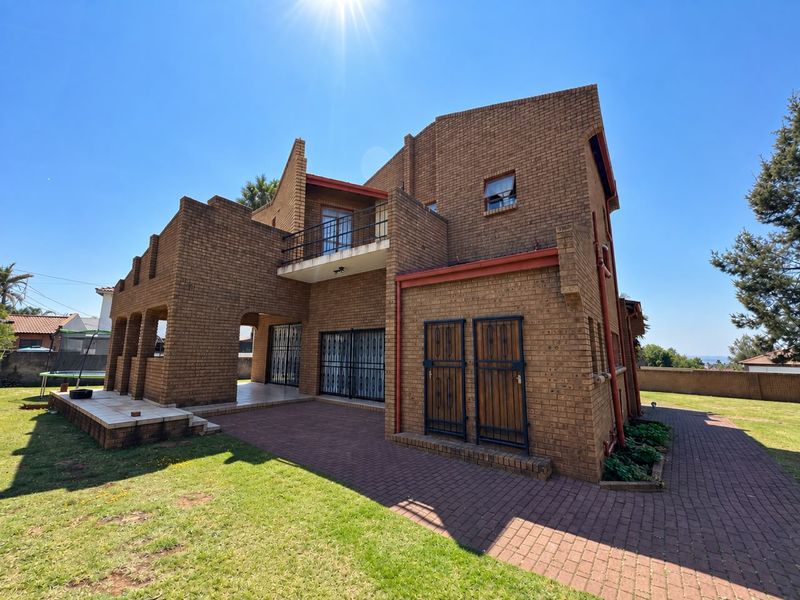 Rear view of a multi-story face brick house featuring a balcony, paved patio area, and established lawn.