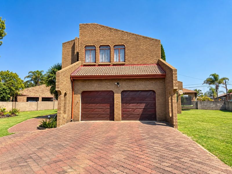 Front view of a double-story brick house featuring a double garage, arched windows, and a spacious paved driveway set within a landscaped garden.