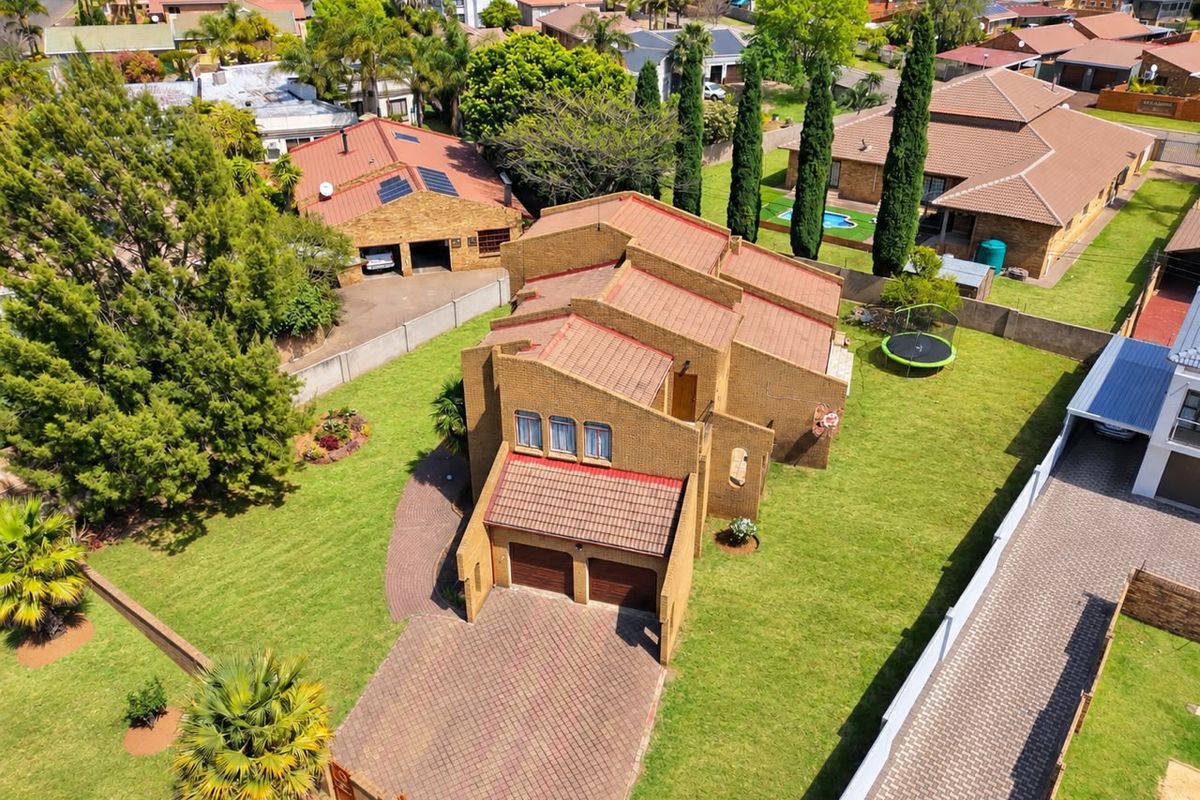 Aerial view of a brick-faced residential property featuring a double garage, paved driveway, and surrounding garden space within a suburban neighborhood.