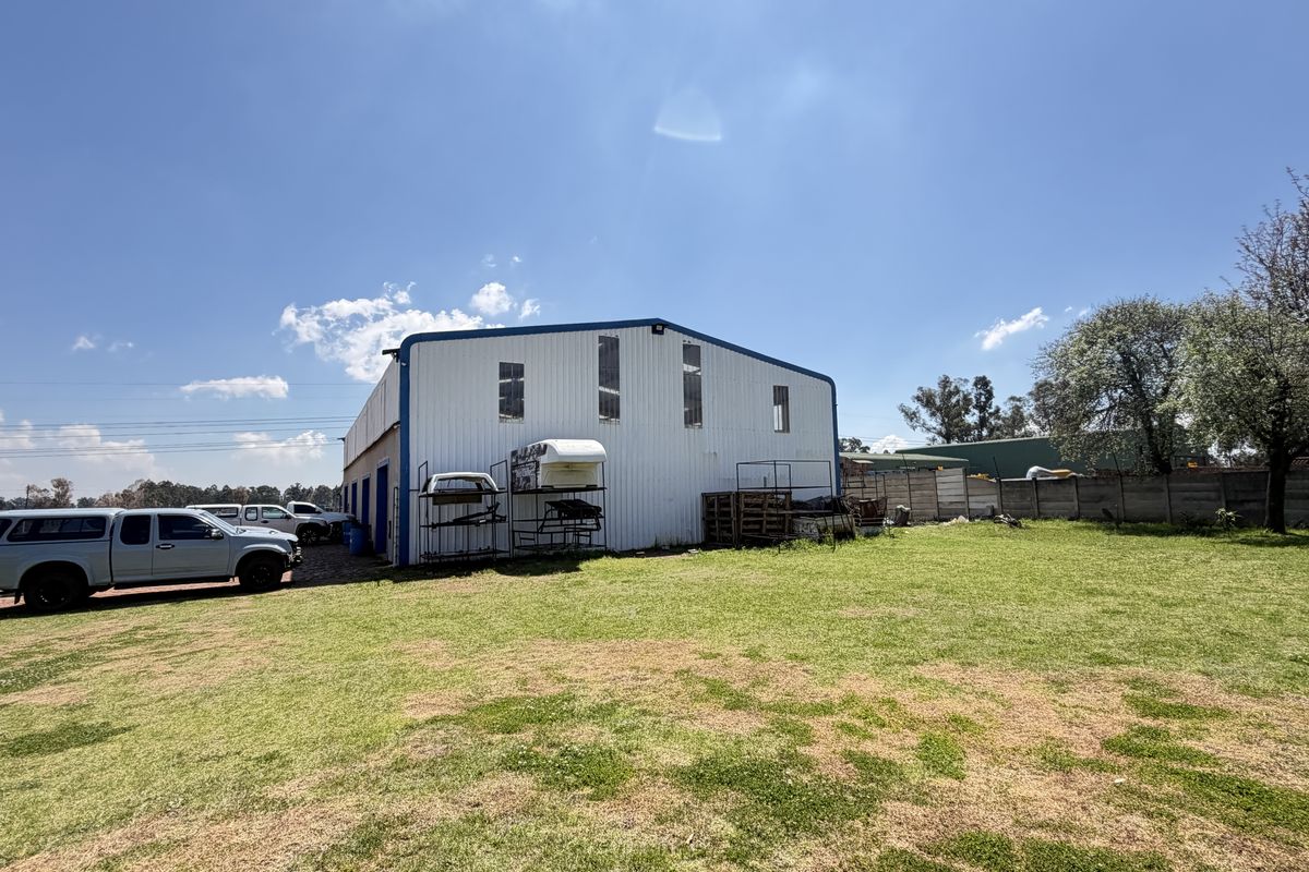Rear view of a large industrial-style metal shed structure situated on a spacious grassed plot with perimeter boundary walling.