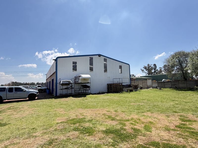 Rear view of a large industrial-style metal shed structure situated on a spacious grassed plot with perimeter boundary walling.