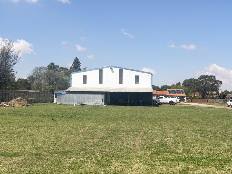 A view of a large corrugated metal shed structure situated on a spacious open lawn with a precast concrete boundary wall.