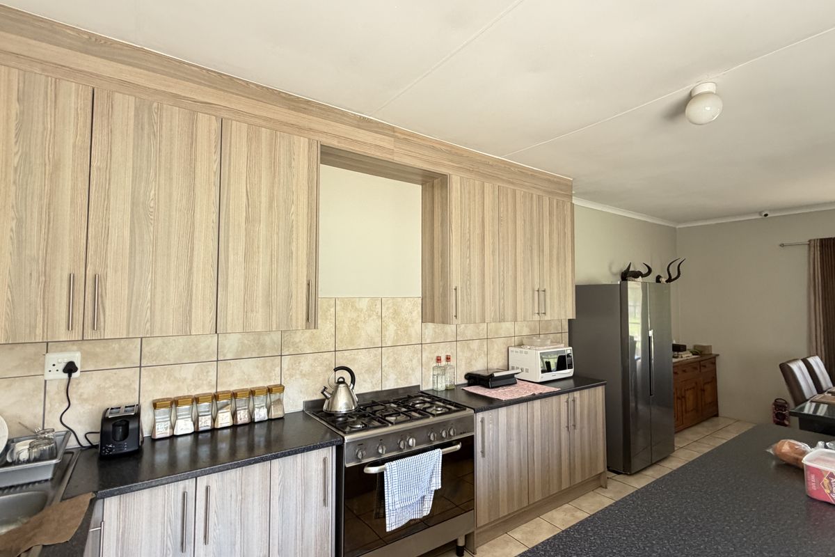 A functional kitchen featuring light wood-grain cabinetry, dark countertops, a gas hob with oven, and a central island, flowing into the dining area.