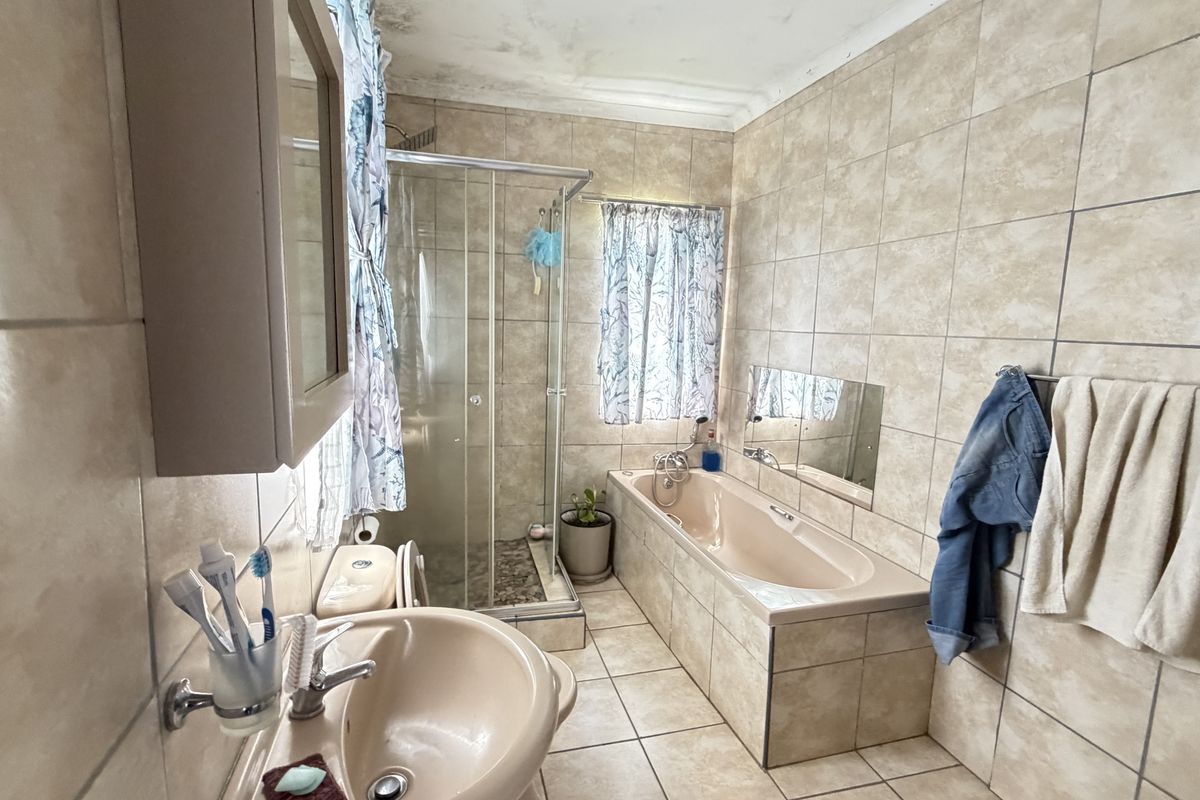 A dated bathroom featuring a built-in bathtub, separate shower enclosure, and tiled finishes, showing signs of ceiling water damage.
