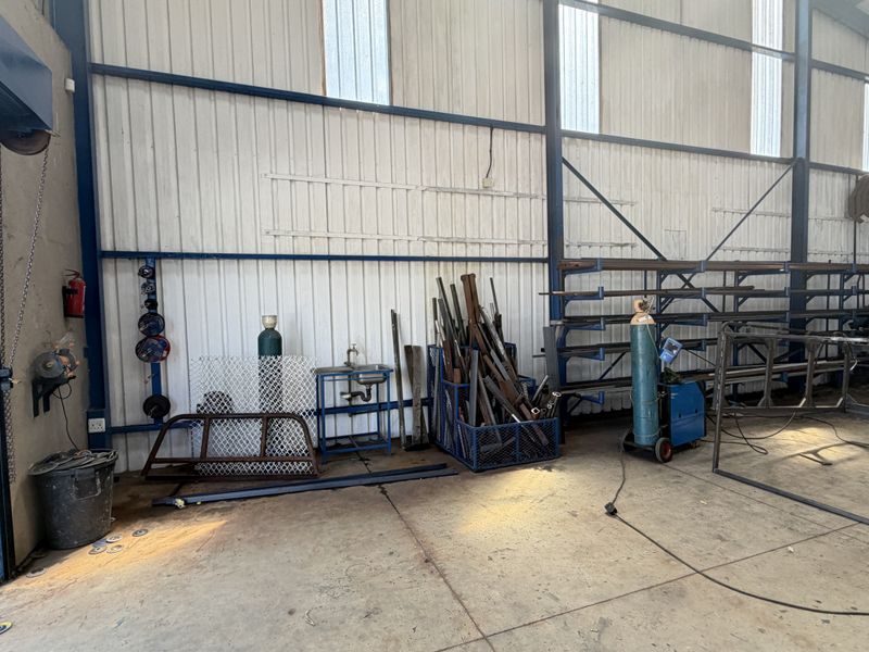 A functional industrial utility space or workshop featuring a steel frame structure, concrete flooring, and integrated metal storage racking for heavy-duty use.