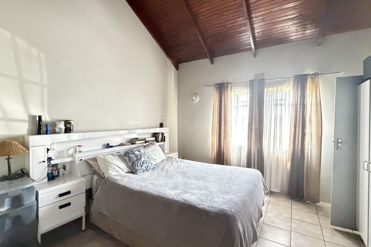 Spacious bedroom featuring a high vaulted timber ceiling, tiled flooring, and a built-in headboard unit.