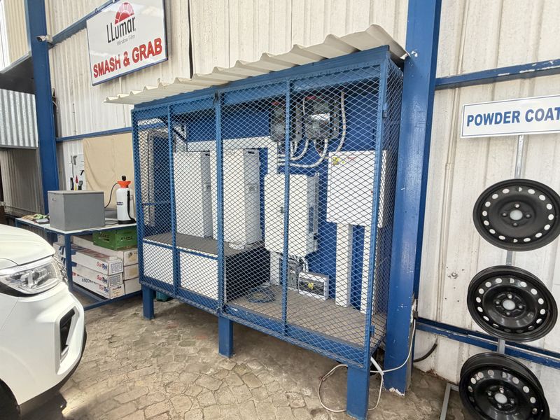 A utility area within a workshop featuring a secured metal cage housing electrical infrastructure, set against corrugated metal walls.