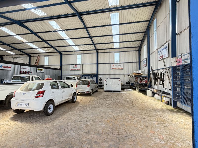 Large industrial-style garage or workshop space featuring a steel portal frame, corrugated metal walls, translucent roof panels, and durable cobblestone flooring.