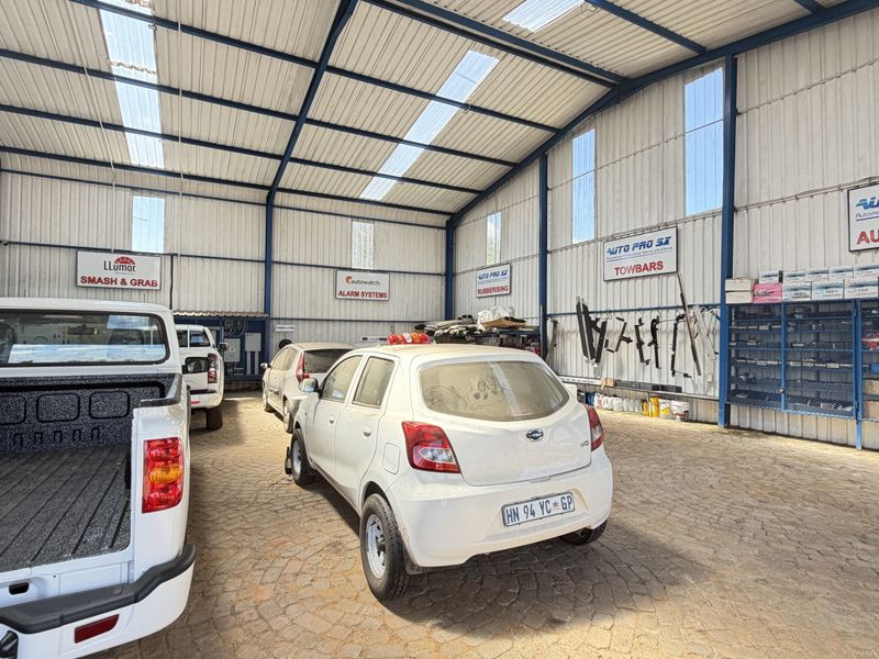 Spacious industrial-style garage or workshop featuring a steel portal frame, corrugated metal walls, translucent roof panels, and extensive built-in metal shelving.