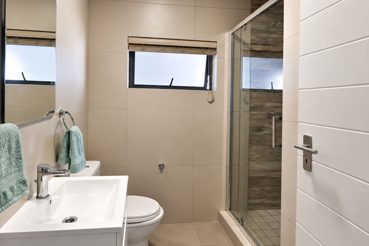 Modern bathroom featuring a vanity basin, toilet, and a glass-enclosed shower with neutral wall and floor tiling.
