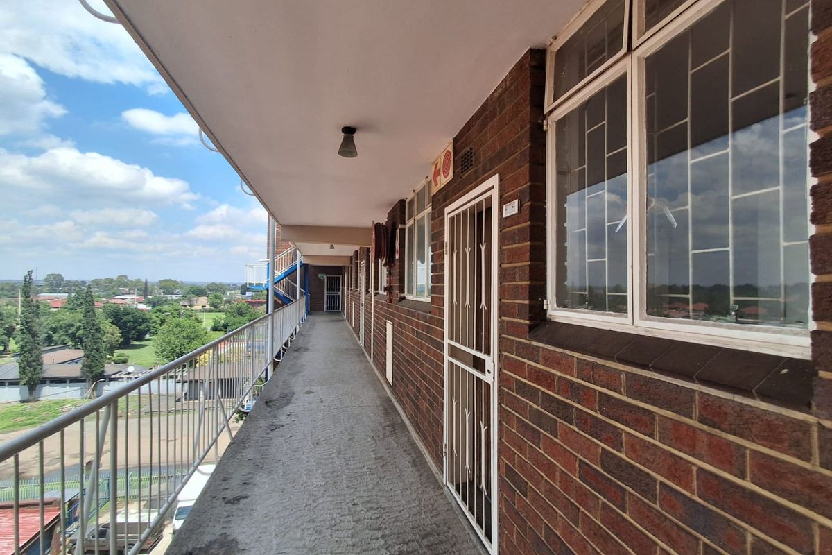 An exterior apartment walkway featuring brick walls, security gates, and metal railings with views over the surrounding area.
