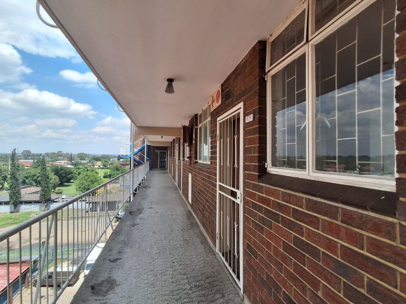 An exterior apartment walkway featuring brick walls, security gates, and metal railings with views over the surrounding area.