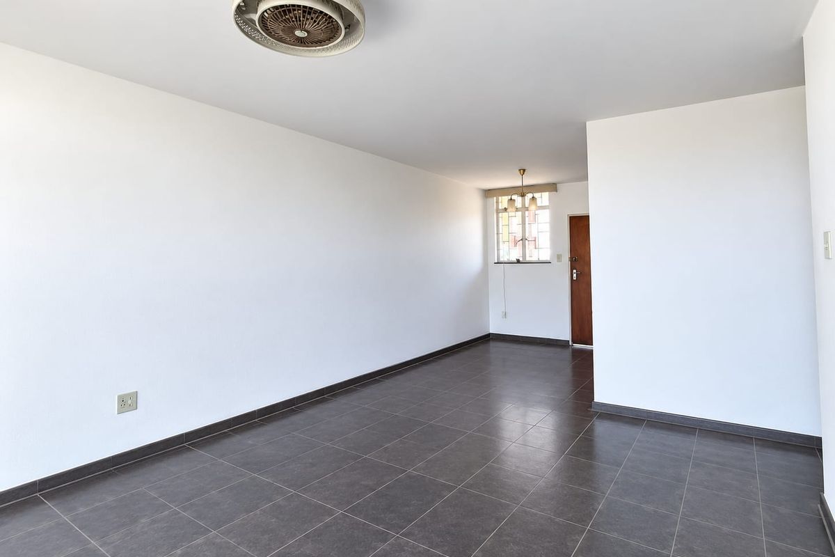 A spacious, empty living area featuring dark tiled flooring, a ceiling fan, and neutral white walls, offering a blank canvas for interior design.