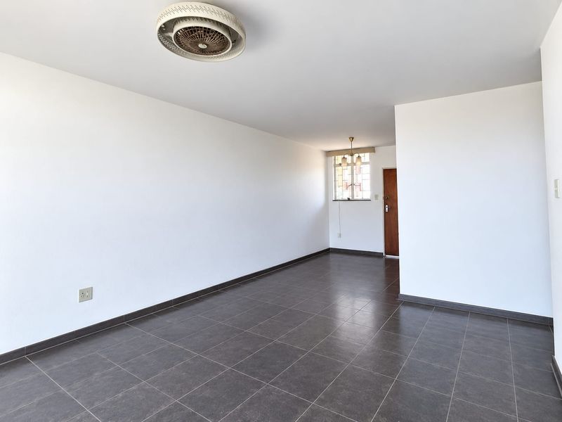 A spacious, empty living area featuring dark tiled flooring, a ceiling fan, and neutral white walls, offering a blank canvas for interior design.